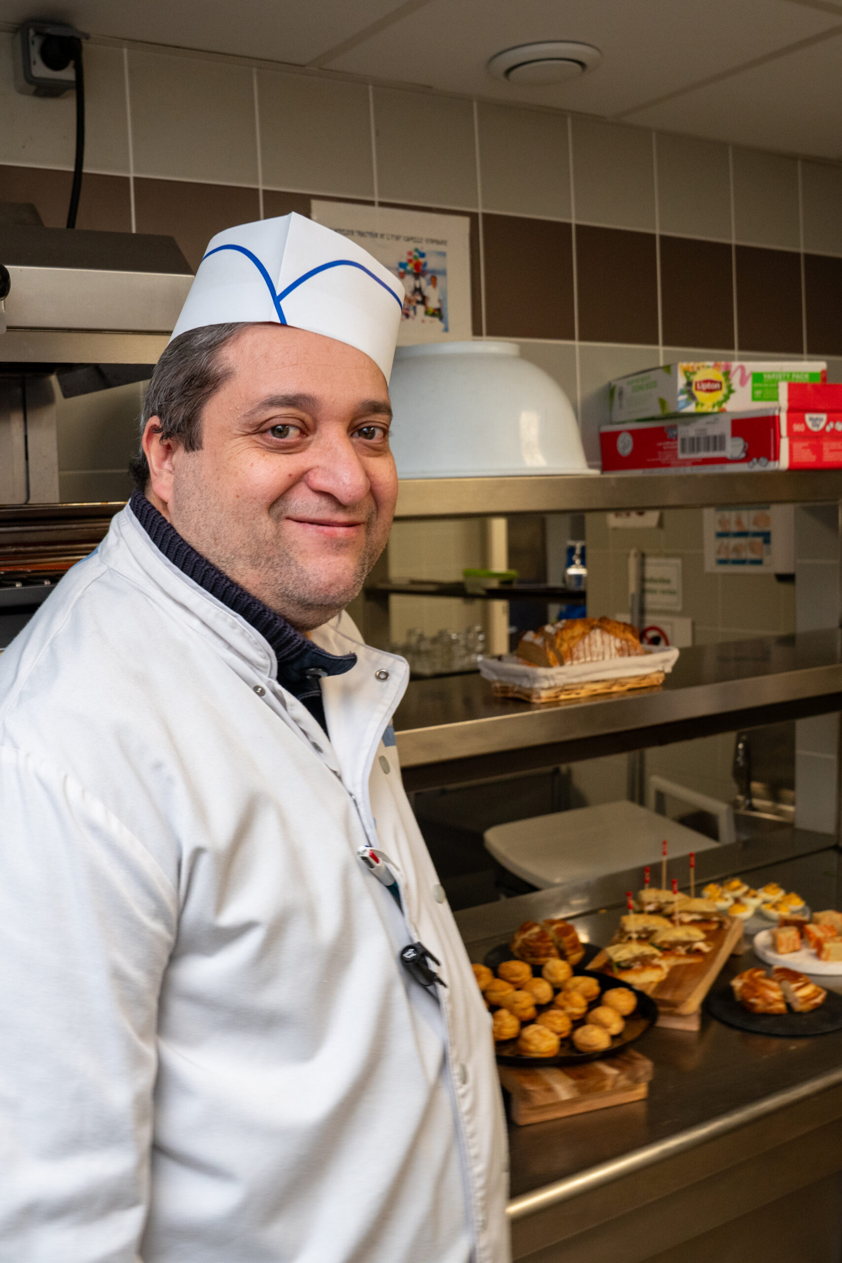 Boubou, travailleur en ESAT, souriant en cuisine chez Fika Traiteur, illustrant l'inclusion et l'impact social de l'entreprise.