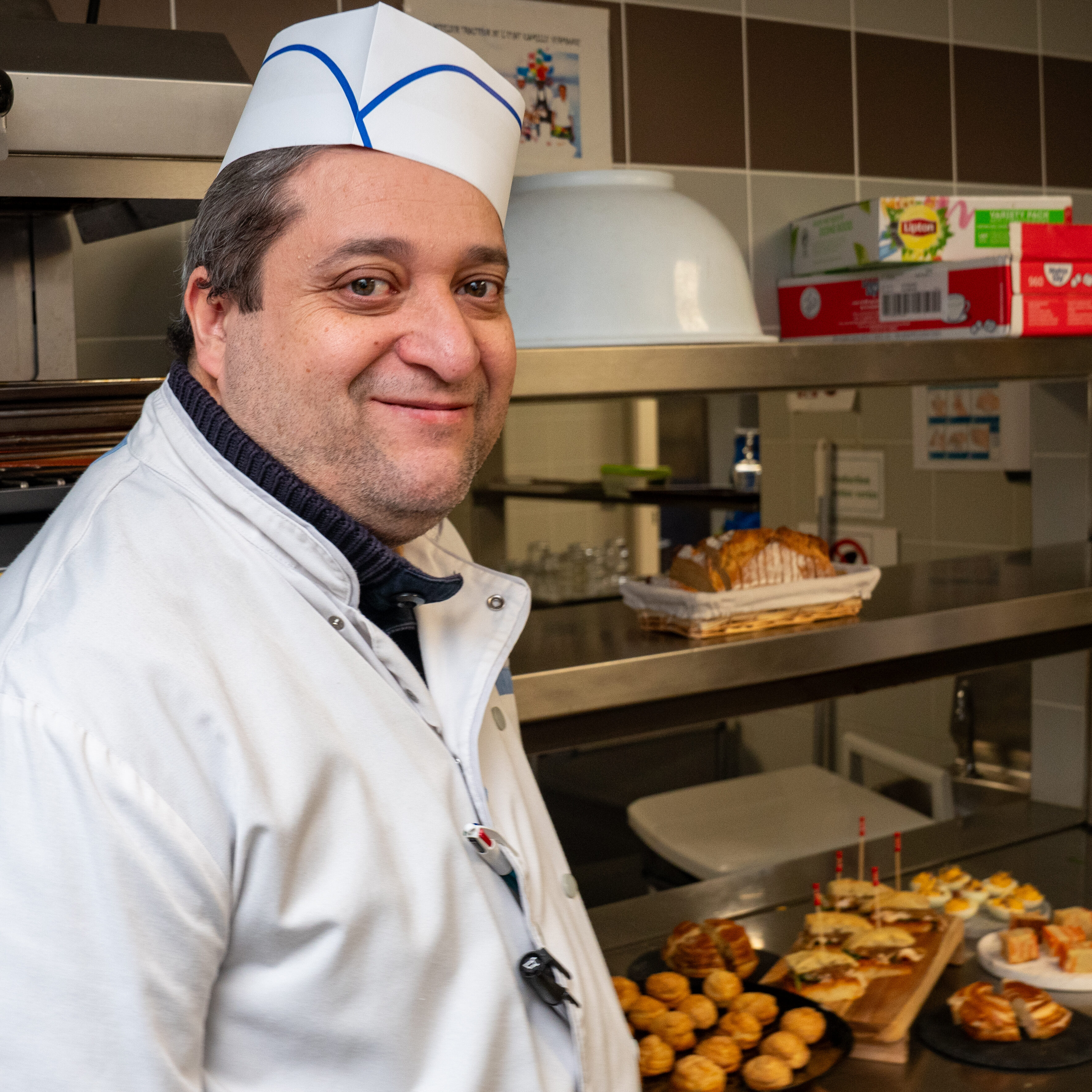 Boubou, travailleur en ESAT, souriant en cuisine chez Fika Traiteur, illustrant l'inclusion et l'impact social de l'entreprise.