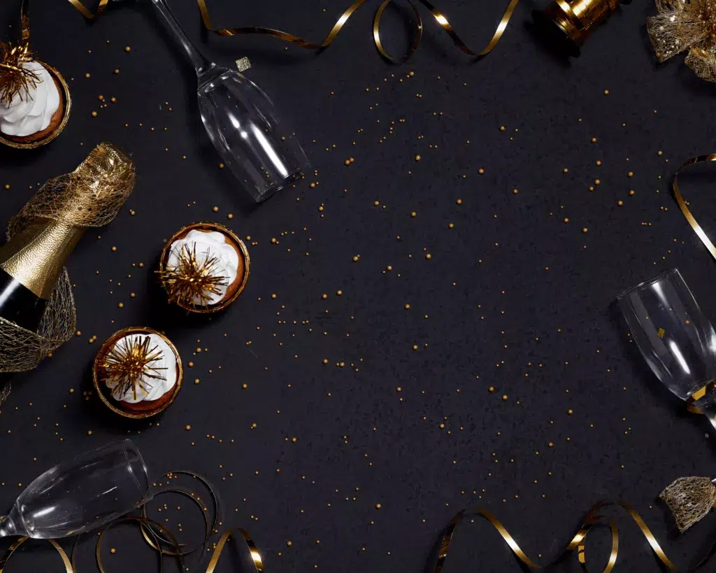 Vue de dessus d’une décoration de Nouvel An sur fond noir : bouteilles de champagne dorées, flûtes vides, cupcakes à la crème blanche décorés d’étoiles dorées, rubans et confettis or, ambiance festive élégante.
Organiser un événement d'entreprise pour fêter la nouvelle année